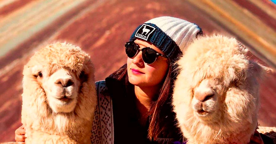 girl with sunglasses between llamas in rainbow mountain Cusco