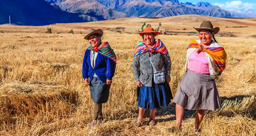 Three women in traditional clothing stand in a lush field under the clear skies of Peru in August.