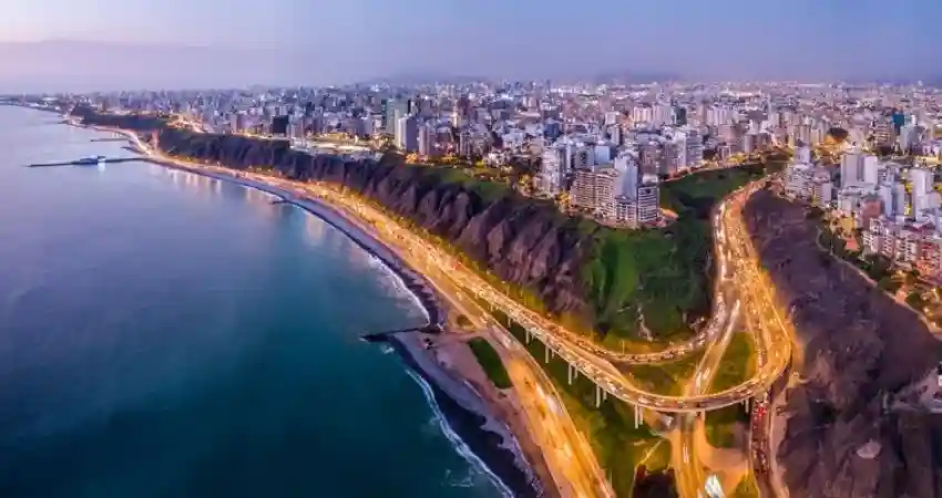 Aerial view of Lima, Peru, showcasing the city's skyline and surrounding mountains under a clear blue sky.