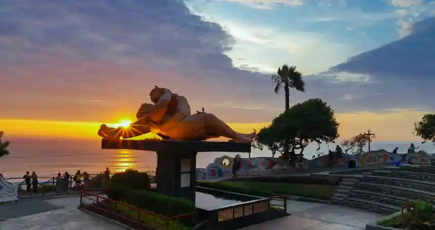 A statue of a man sitting on a bench at sunset in Love Park, Lima, Peru, with warm hues illuminating the scene.