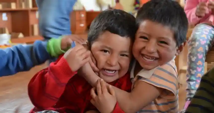 Two smiling children embrace each other warmly, showcasing joy and connection during a volunteer event in Cusco, Peru.