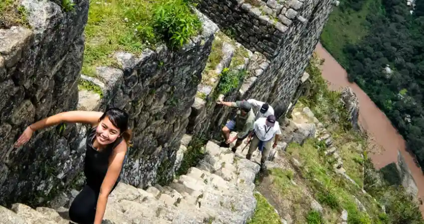 A woman climbing the steep stone steps of Machu Picchu, known as the death stairs, surrounded by ancient ruins.