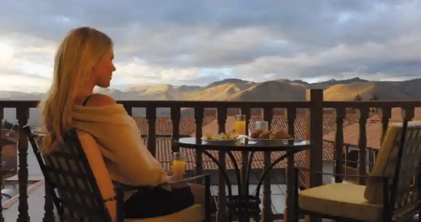 A woman seated at a table, enjoying a mountain view, highlighting luxury accommodations in Cusco.