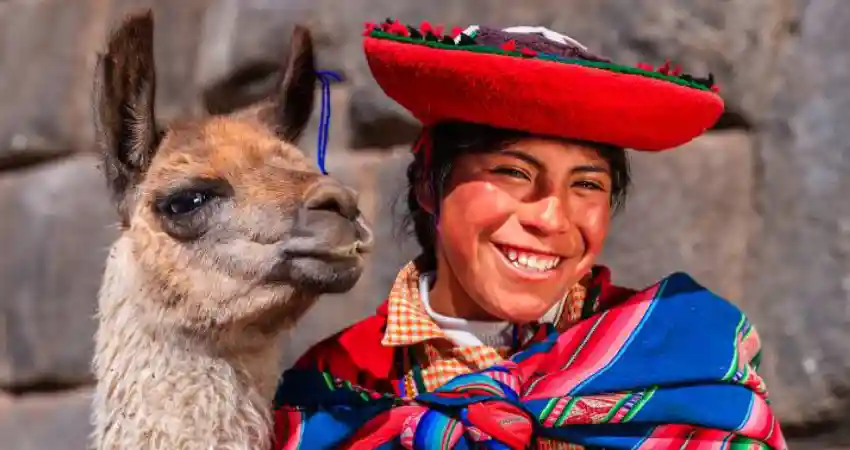 A smiling woman in traditional clothing poses with a llama, representing cultural heritage in Peru travel itinerary.