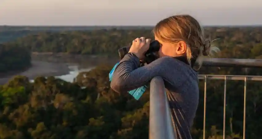 A young girl photographs a river at Posada Amazonas Lodge, surrounded by lush greenery and natural beauty.