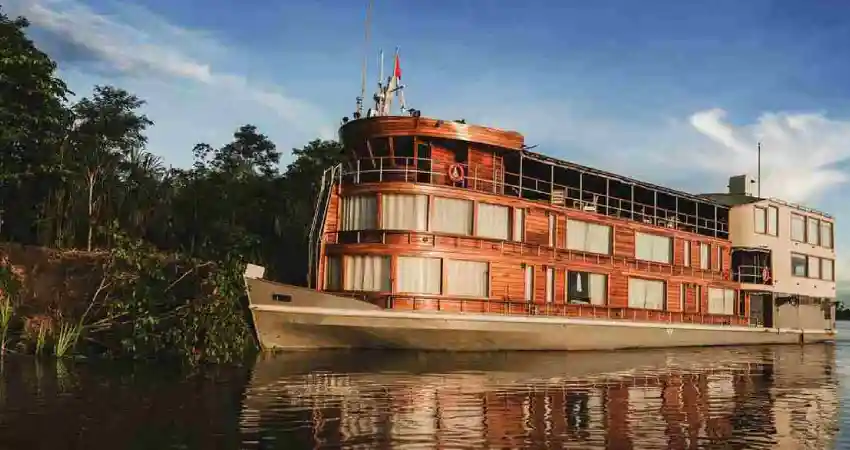 A large boat named Pure Amazon Cruise on the water, surrounded by lush trees in the background.