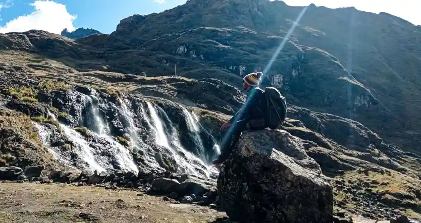 A man sits on a rock beside a waterfall, enjoying the scenic beauty of one of Peru's best trekking locations.