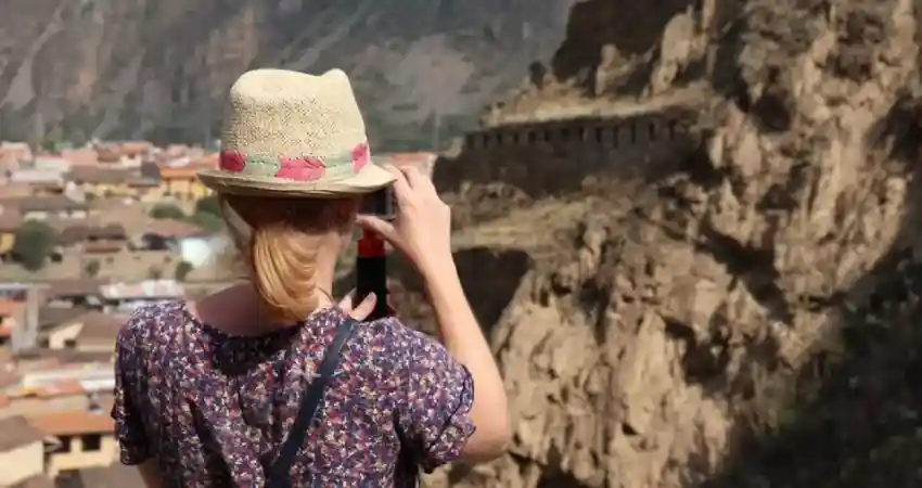 A woman in a hat captures a photo of a mountain while enjoying a Cusco Luxury Tours experience.