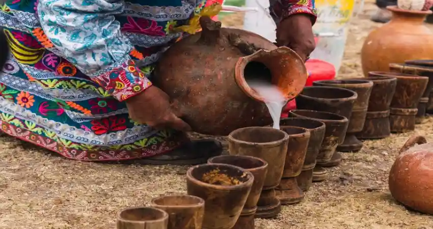 A woman pours milk into a wooden pot, showcasing a traditional practice related to custom Peru packages.