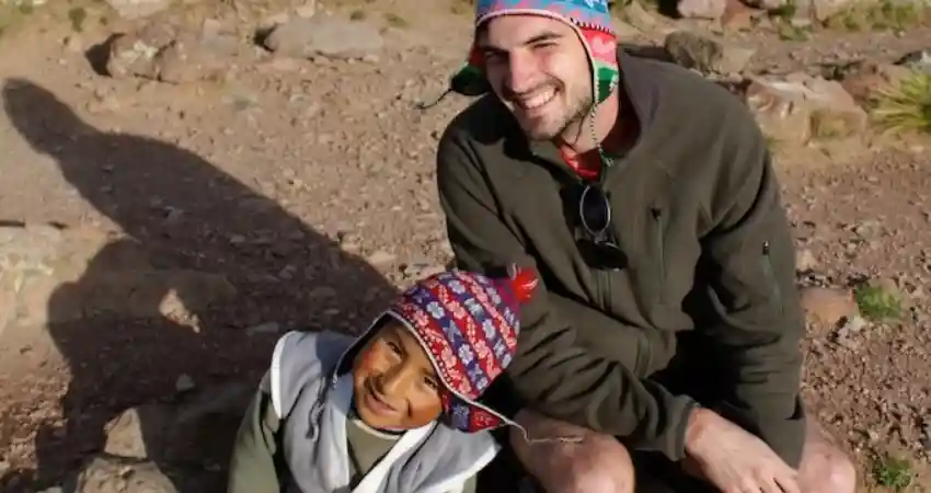 A man and a child sit on rocks, enjoying multi-generational travel in Peru, surrounded by scenic landscapes.
