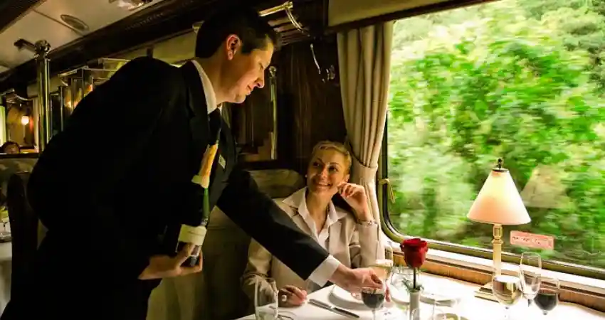 A man in a suit serves a woman on a train, highlighting luxury travel experiences in Peru.