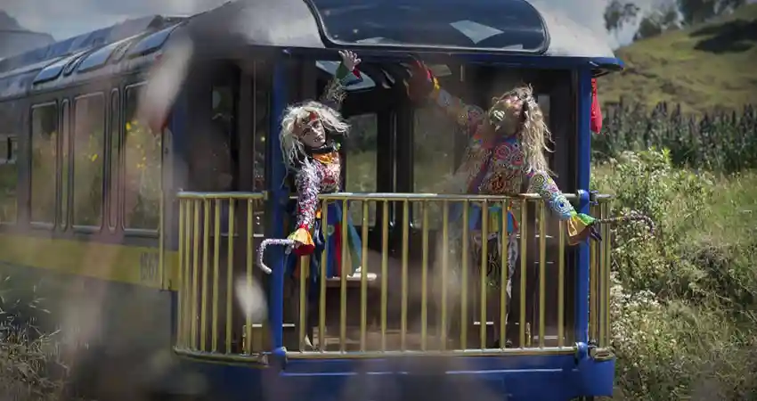 Two clowns stand beside a train, promoting Peru VIP Travel with colorful outfits and playful expressions.