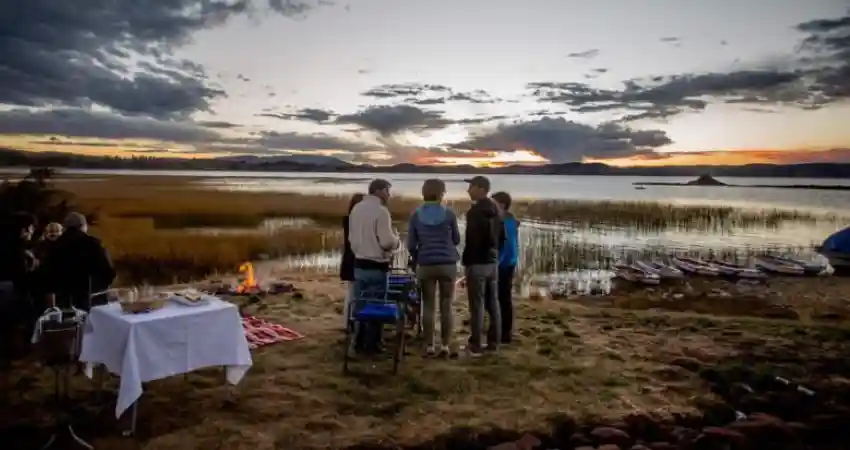 A group of people gathered around a table by the lake at Titilaka Lodge, enjoying a scenic outdoor setting.