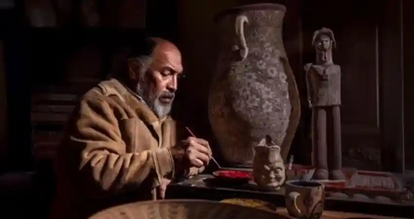 An elderly man sits at a table in the Ceramic Workshop Cusco, surrounded by a bowl and decorative vases.