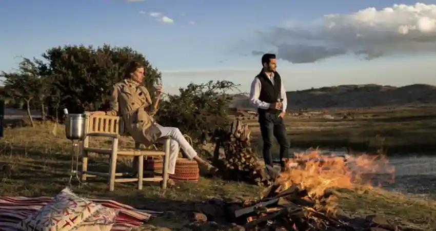 A man and woman sit by a campfire, enjoying the serene view of a lake during their custom Peru itinerary.