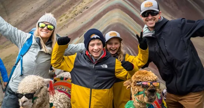 A family poses with alpacas on a mountain during their travel in Peru, surrounded by scenic landscapes.