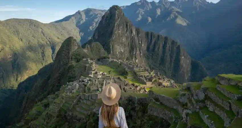 A woman in a hat stands on a hill, gazing at the ancient ruins of Machu Picchu in Peru.