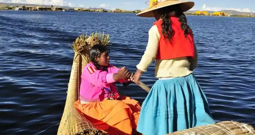 Two women in vibrant clothing enjoy a luxury boat trip on water, reflecting a scenic view of Peru.