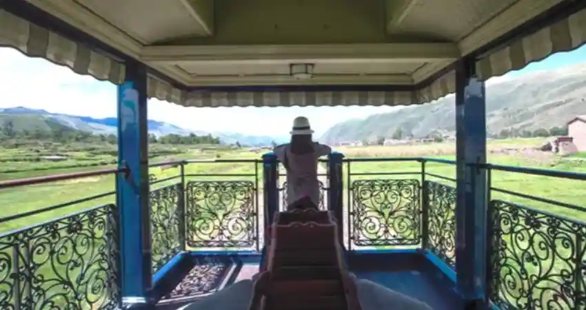 A person stands on a train balcony, enjoying scenic views while traveling on a luxury train in Peru.