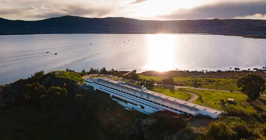 Aerial view of the GHL Lake Titicaca Luxury Hotel, a large white building situated on a scenic hill.