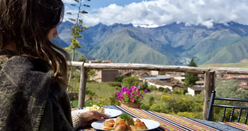A woman enjoys a meal at a table with the Iskay Maras mountains in the background.