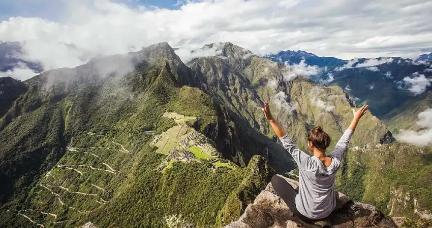 A woman sits on a mountain edge, gazing at the valley below from the heights of Huayna Picchu.