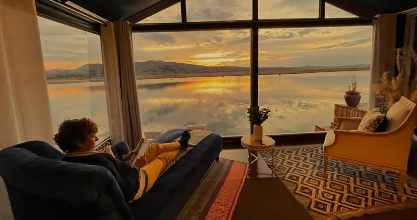 A man sits in a chair by a window, gazing at the water outside at Lake Titicaca Lodge.