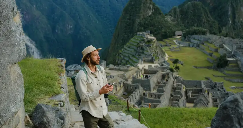 A man in a hat stands on a hill, gazing at the ancient ruins of Machu Picchu during a luxury guided tour in Peru.