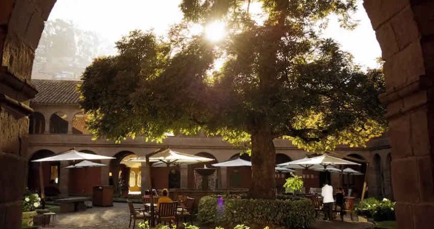Courtyard of Monasterio a Belmond Hotel Cusco featuring a central tree surrounded by elegant stone architecture.