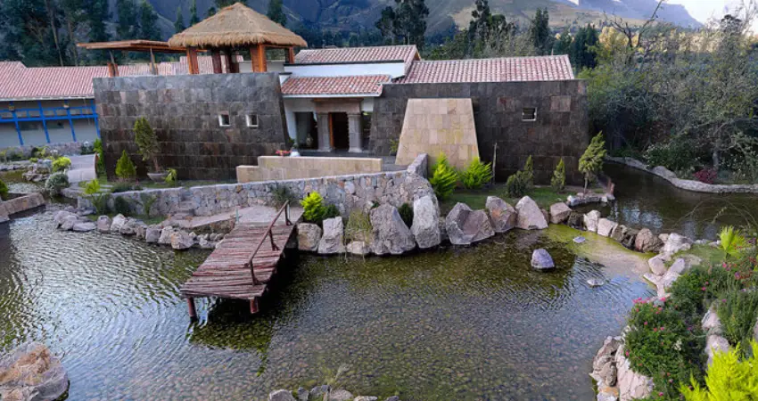 A house with a pond and a bridge in front, set in the scenic Aranwa Sacred Valley.