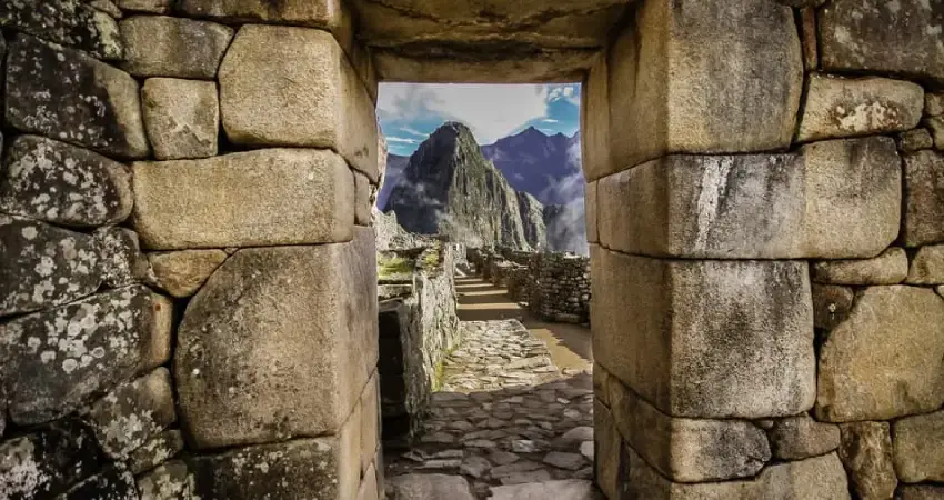 Ancient stone doorway framing a breathtaking view of Machu Picchu's ruins and lush mountains under a clear blue sky.