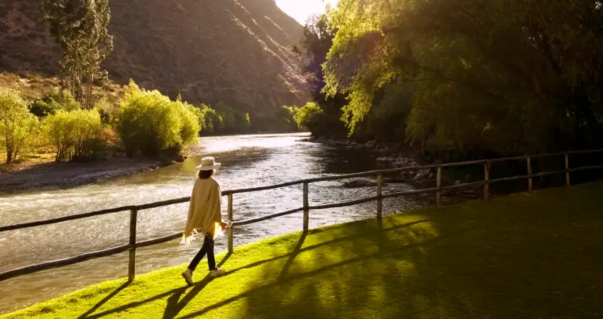 A woman strolls along a riverbank in the mountains, showcasing the scenic beauty of Belmond Hotels in Perú.