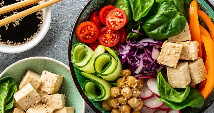 A bowl of vegan Peruvian food featuring tofu, carrots, cucumbers, and assorted vegetables.